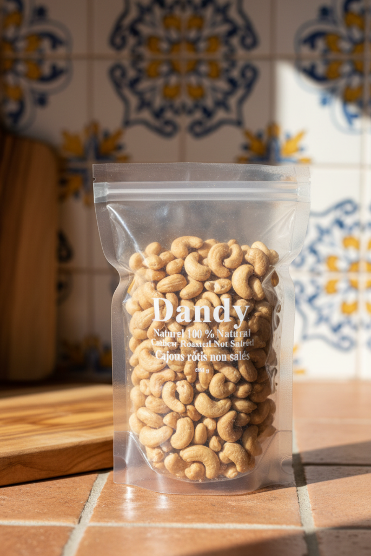Packaged cashew nuts in a clear plastic bag with a white label that has 'Dandy' branding and text stating 'Natural 100% Roasted Not Salted Cashew Nuts'. The net weight is indicated as 1 kg.