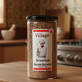 A clear plastic jar labeled 'VILLAGE SARRASSIN KASHA' with a black lid, containing roasted buckwheat seeds.