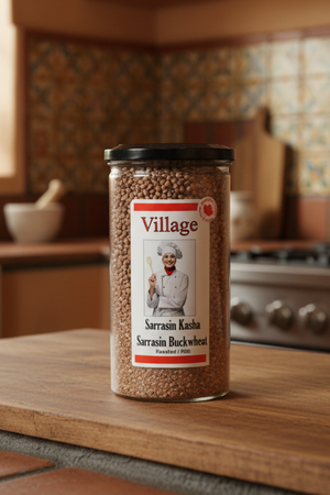 A clear plastic jar labeled 'VILLAGE SARRASSIN KASHA' with a black lid, containing roasted buckwheat seeds.