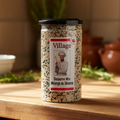 A clear plastic container labeled 'Village' with 'Sesame Mix, Mélange de Sésame' on the label, featuring an image of a chef. The container is filled with black and white sesame seeds.